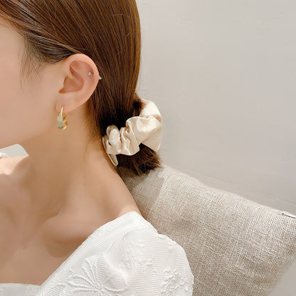 Woman wearing a beige scrunchie in her hair with a neutral background