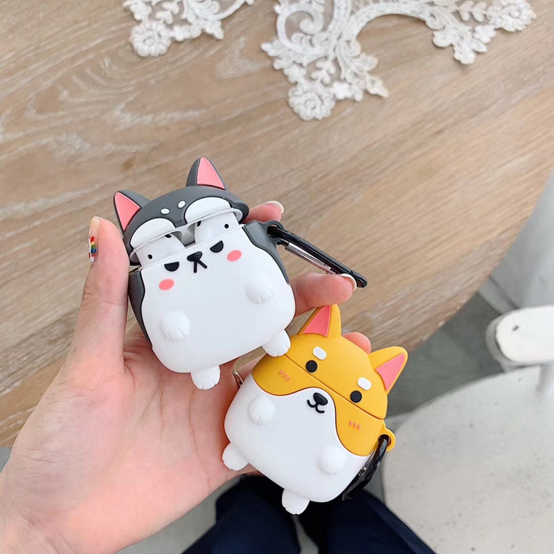 Hand holding two cartoon dog-shaped air pod cases on a wooden surface with decorative elements.